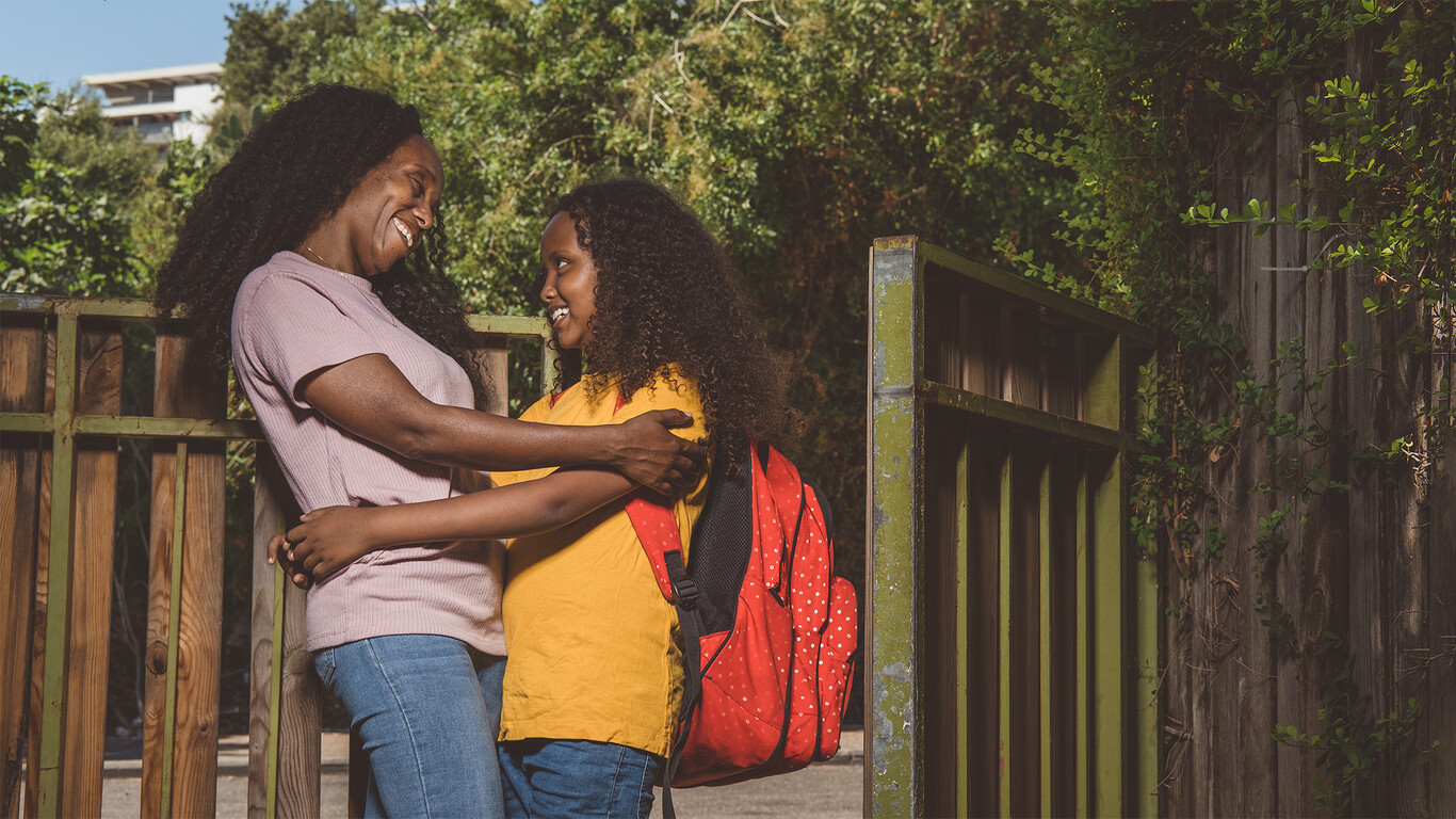 A girl with a backpack and a woman are hugging.