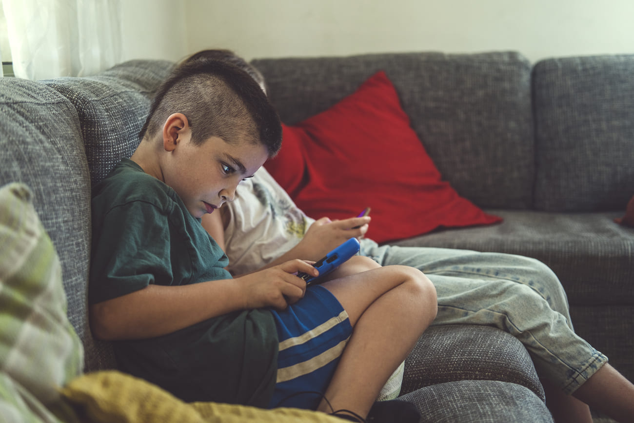 Children are sitting on the couch, using a mobile phone.