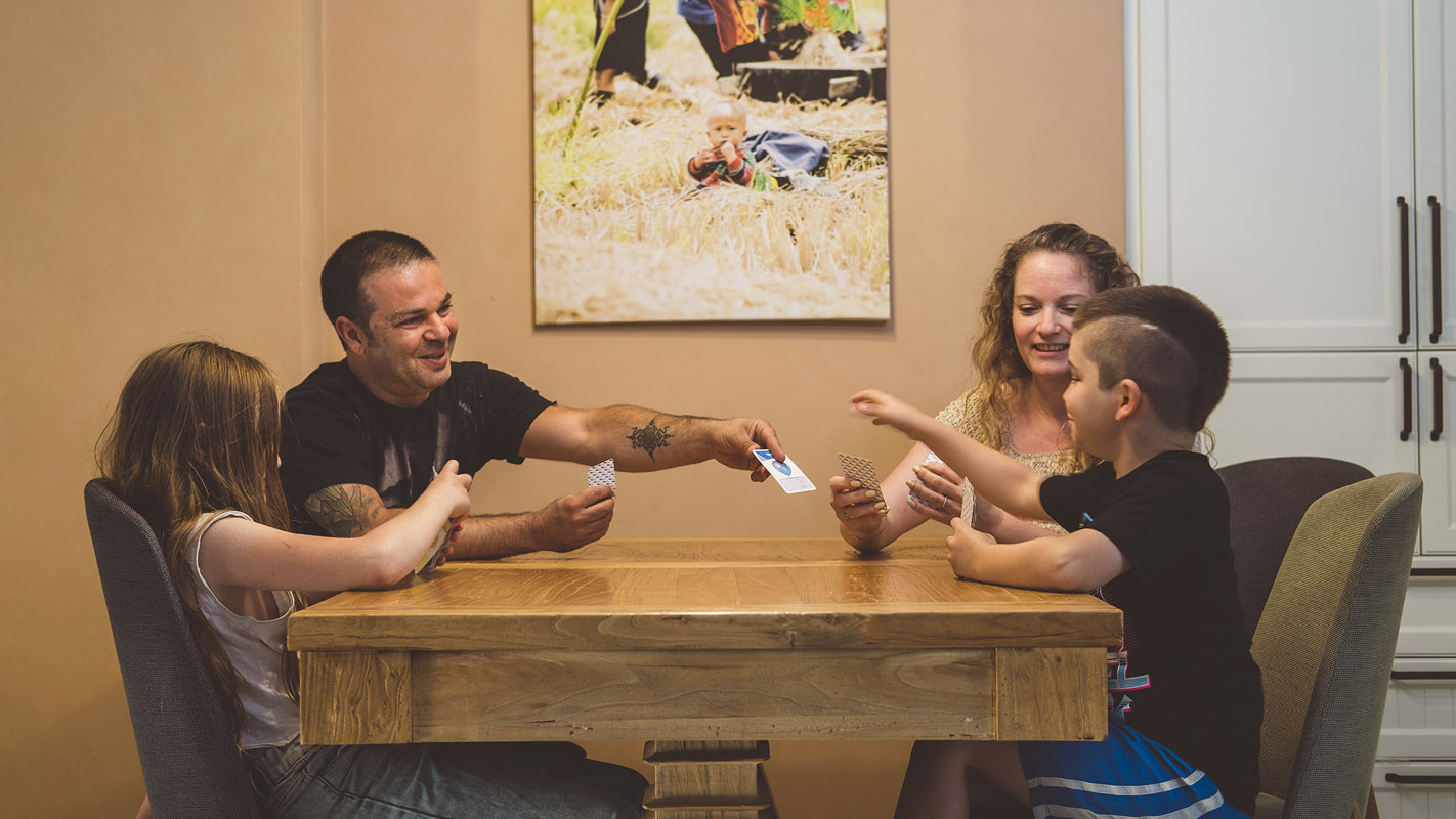 זוג ושני ילדים יושבים מסביב לשולחן ומשחקים בקלפים