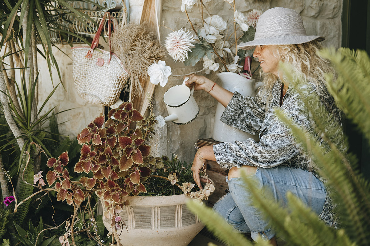 A woman kneels, watering a potted plant with a watering can.