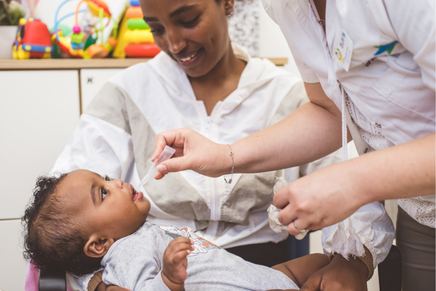 امرأة تحمل طفلها في مركز رعاية الأم والطفل، بينما تعطيه الممرضة قطرات عن طريق الفم