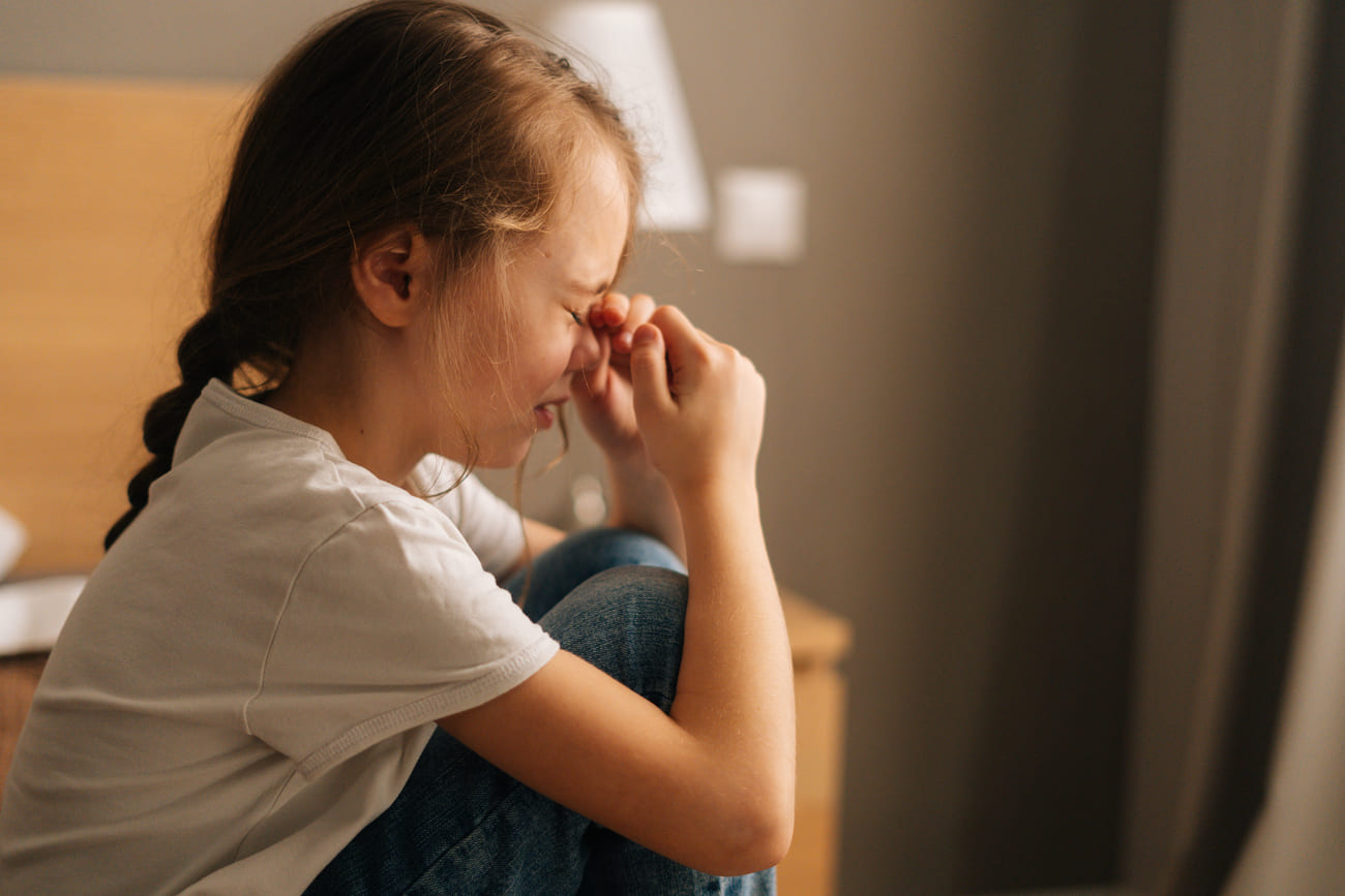 A girl is sitting with her face in her hands.