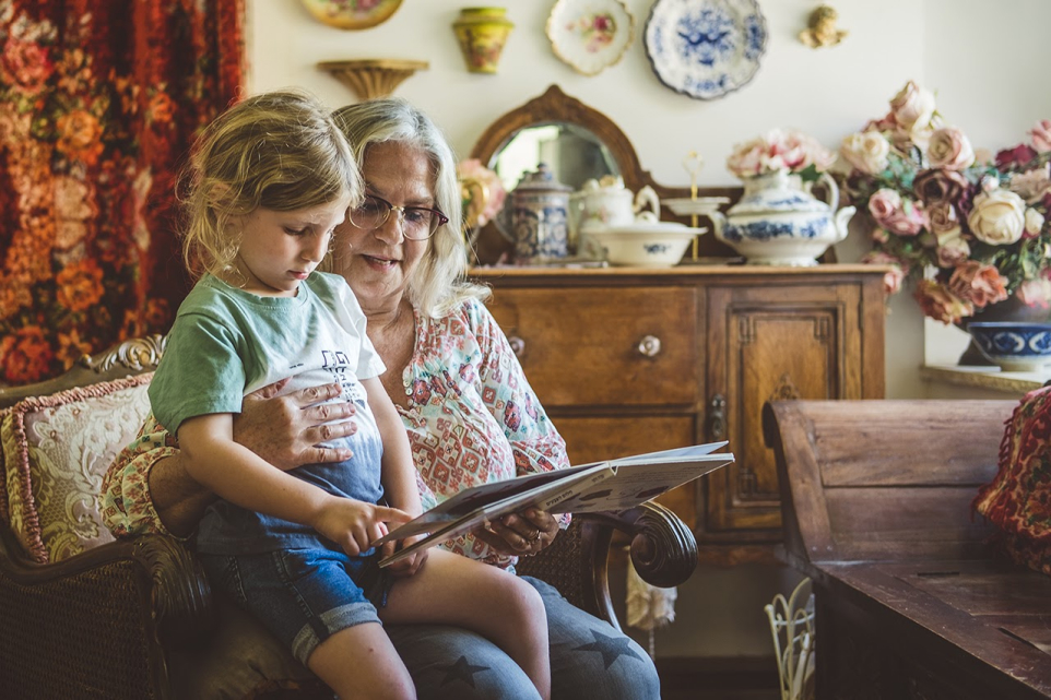 סבתא מקריאה סיפור לנכדה שיושבת על הברכיים שלה
