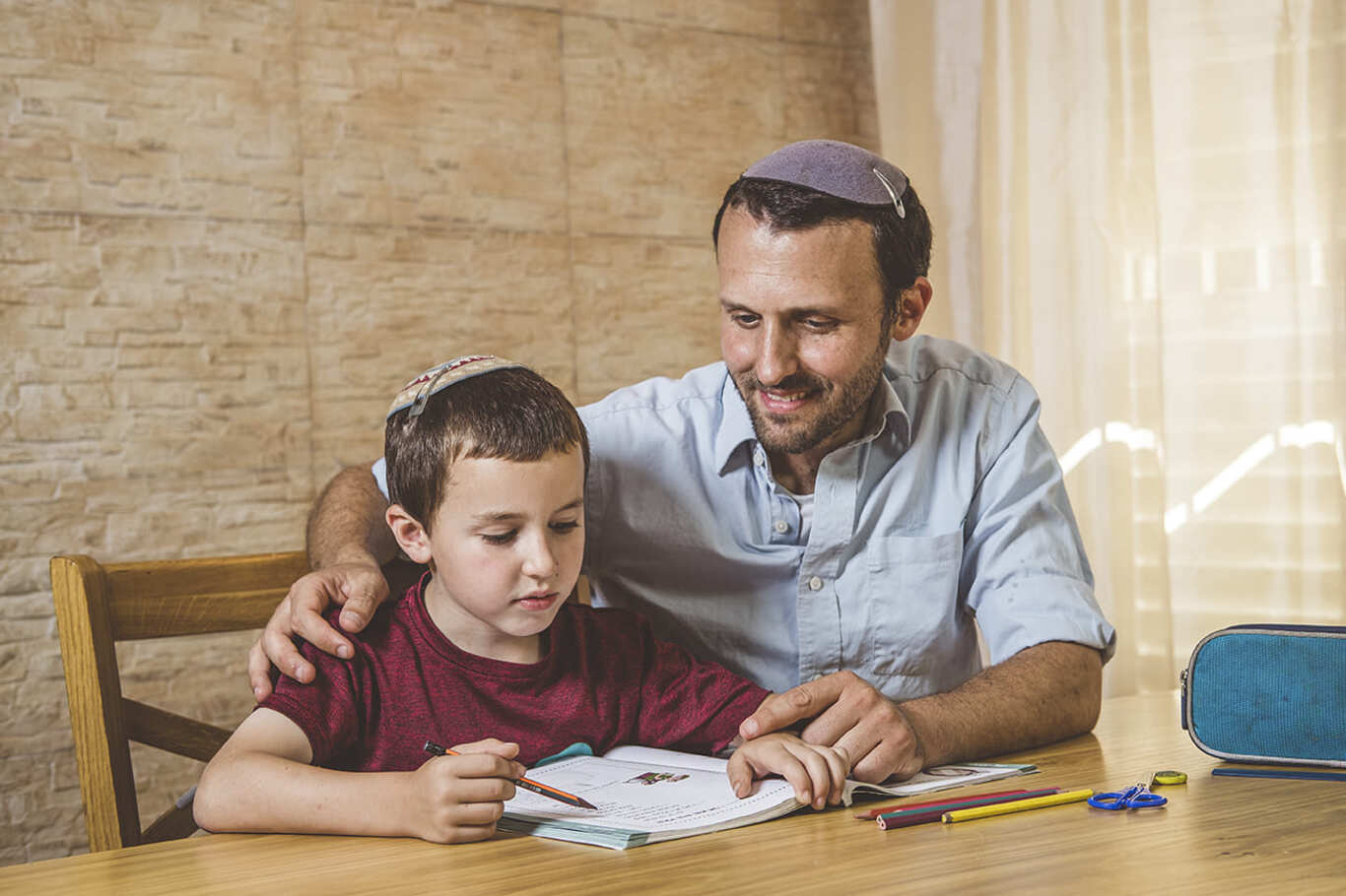 גבר צעיר וילד יושבים ליד שולחן והילד קורא וכותב בספר