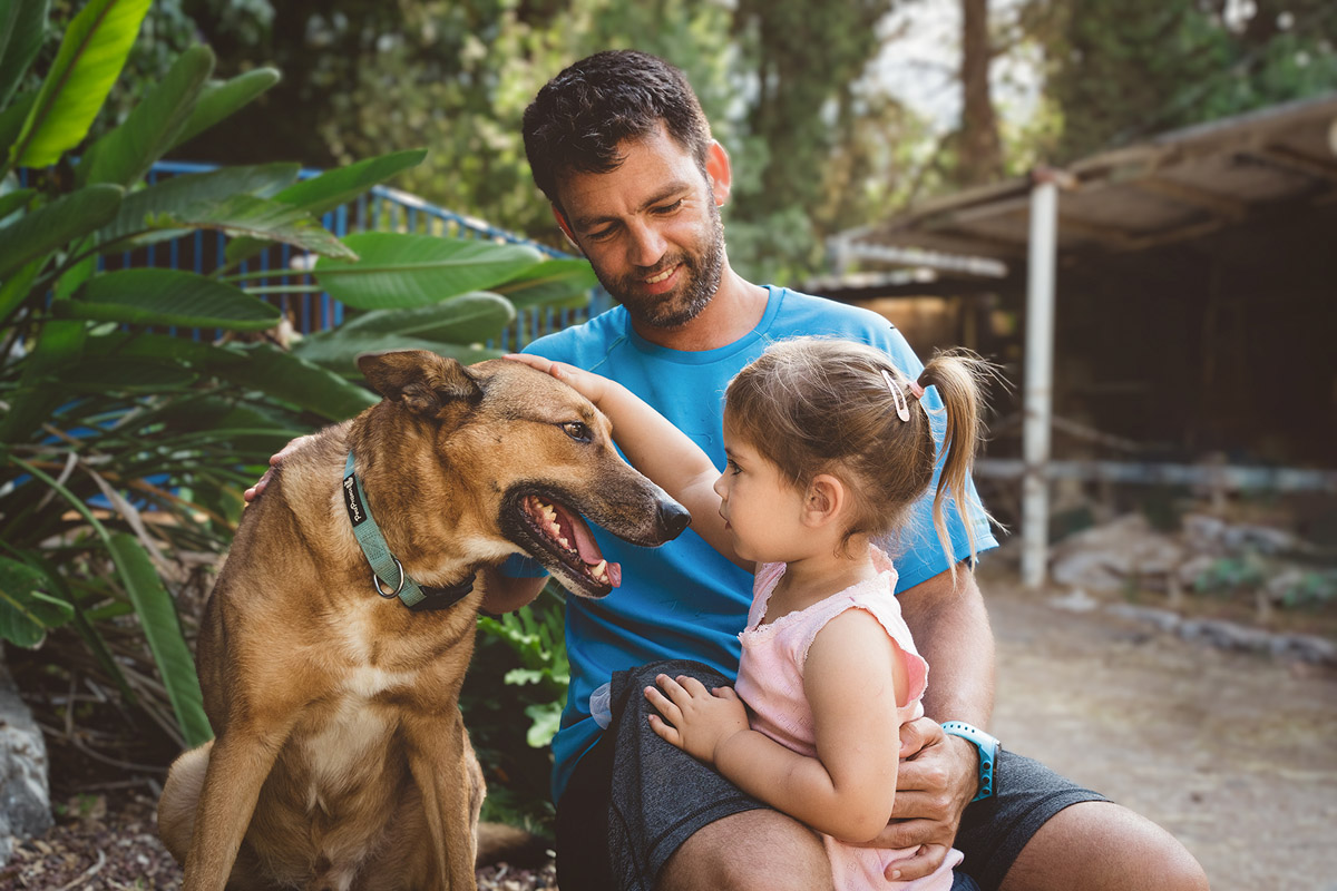 גבר צעיר מחבק ילדה שמלטפת כלב