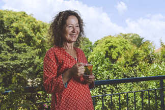 אישה מחזיקה כוס תה ומחייכת, ברקע עצים