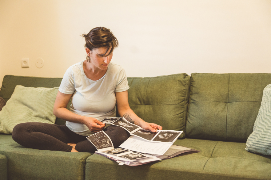 אישה בהריון יושבת על ספה ומסתכלת על תוצאות בדיקת האולטרסאונד שלה