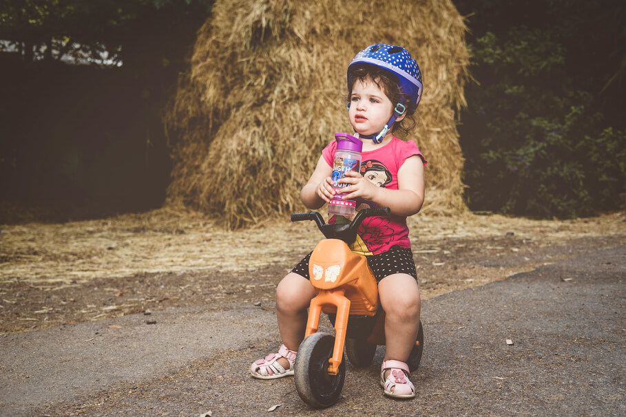 Toddler with a helmet sitting on a small bike and drinking water