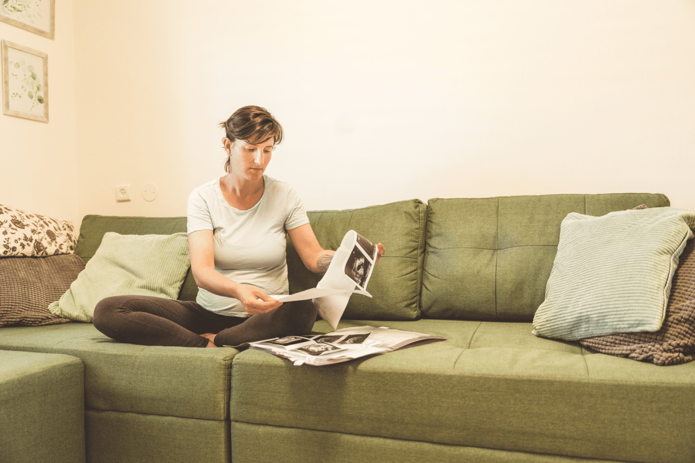 אישה בהריון יושבת על ספה מול דפי בדיקות הריון