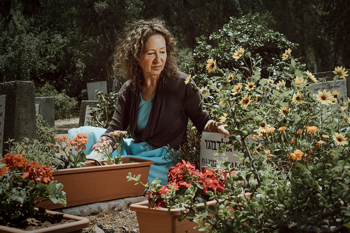 An elderly woman is sitting next to a gravestone.