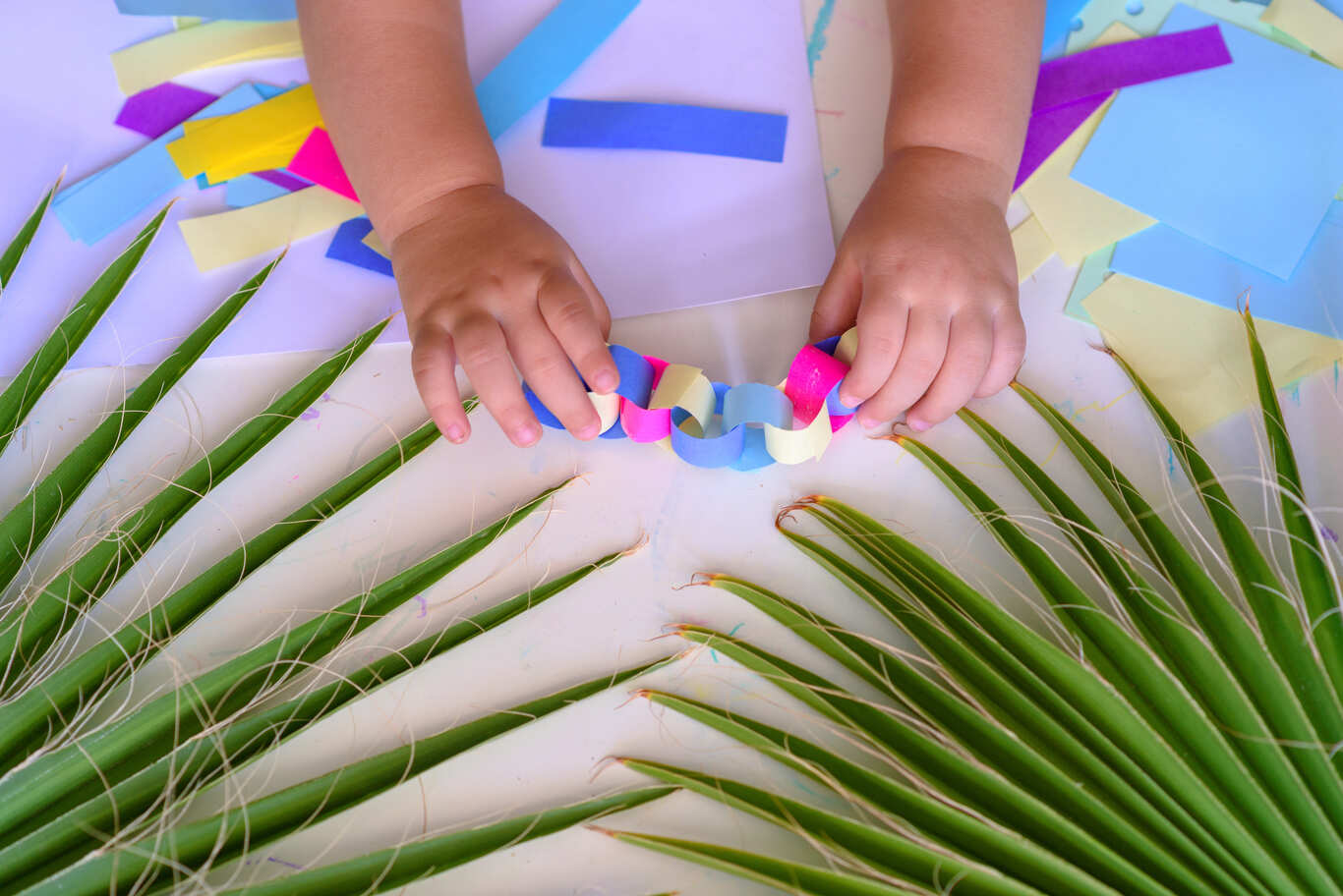 A toddler's hands are making decorations for the Sukkah.