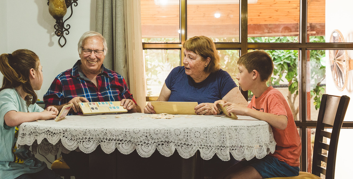 שני מבוגרים בגיל השלישי ושני ילדים יושבים מסביב לשולחן ומחייכים