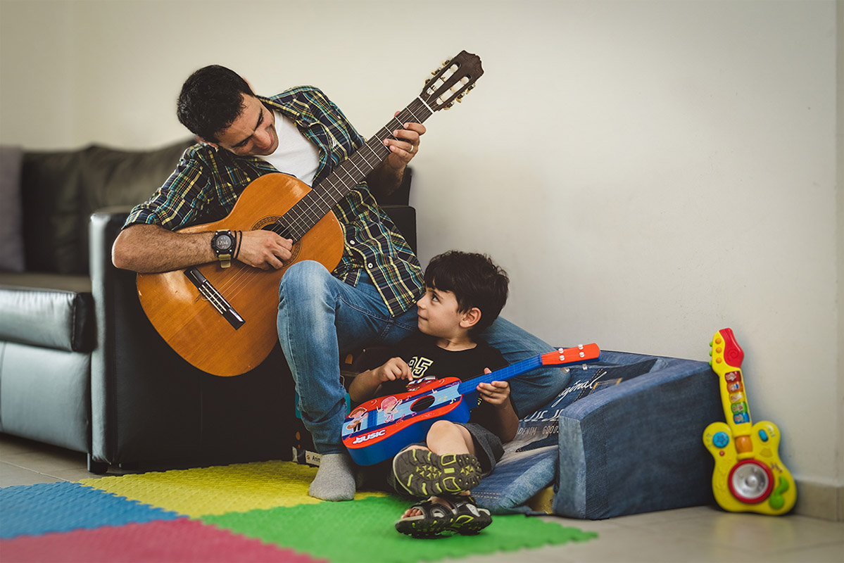 A man is playing guitar, and a child is playing with a toy guitar.