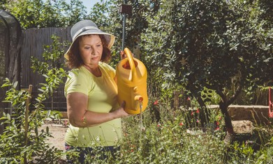 An elderly woman is watering the garden with a watering can.